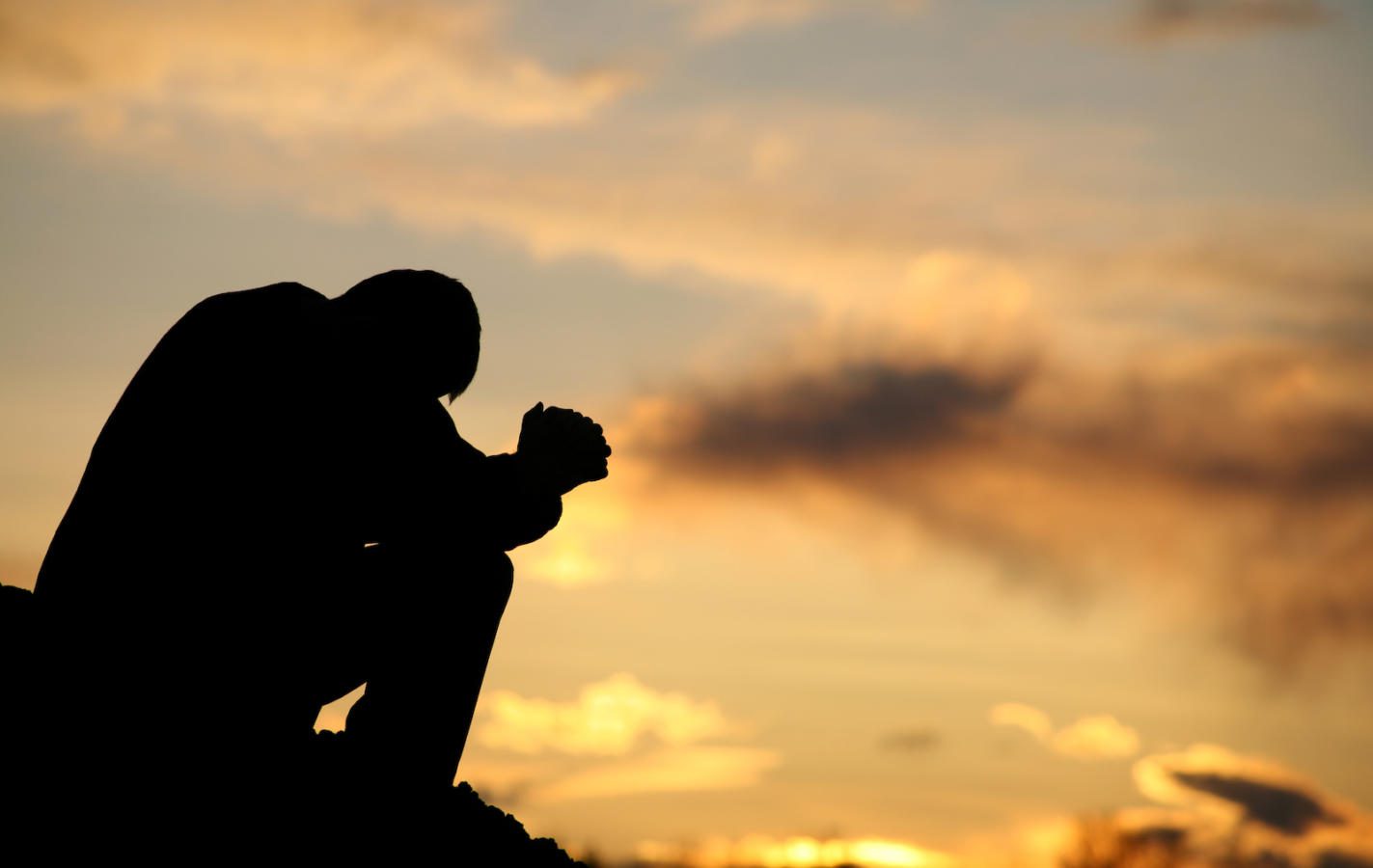 A silhouette of a man praying at sunset. Model is handsome Caucasian male in his 30s with unrecognizable side view. Model is folding his hands and bowing his head. Themes include meditation, spirituality, balance, freedom, vitality, hope, hurt, problems, addiction, struggle, anguish, help, god, healing, recovery, perseverance, coping, courage, strength, men, and asking for help.